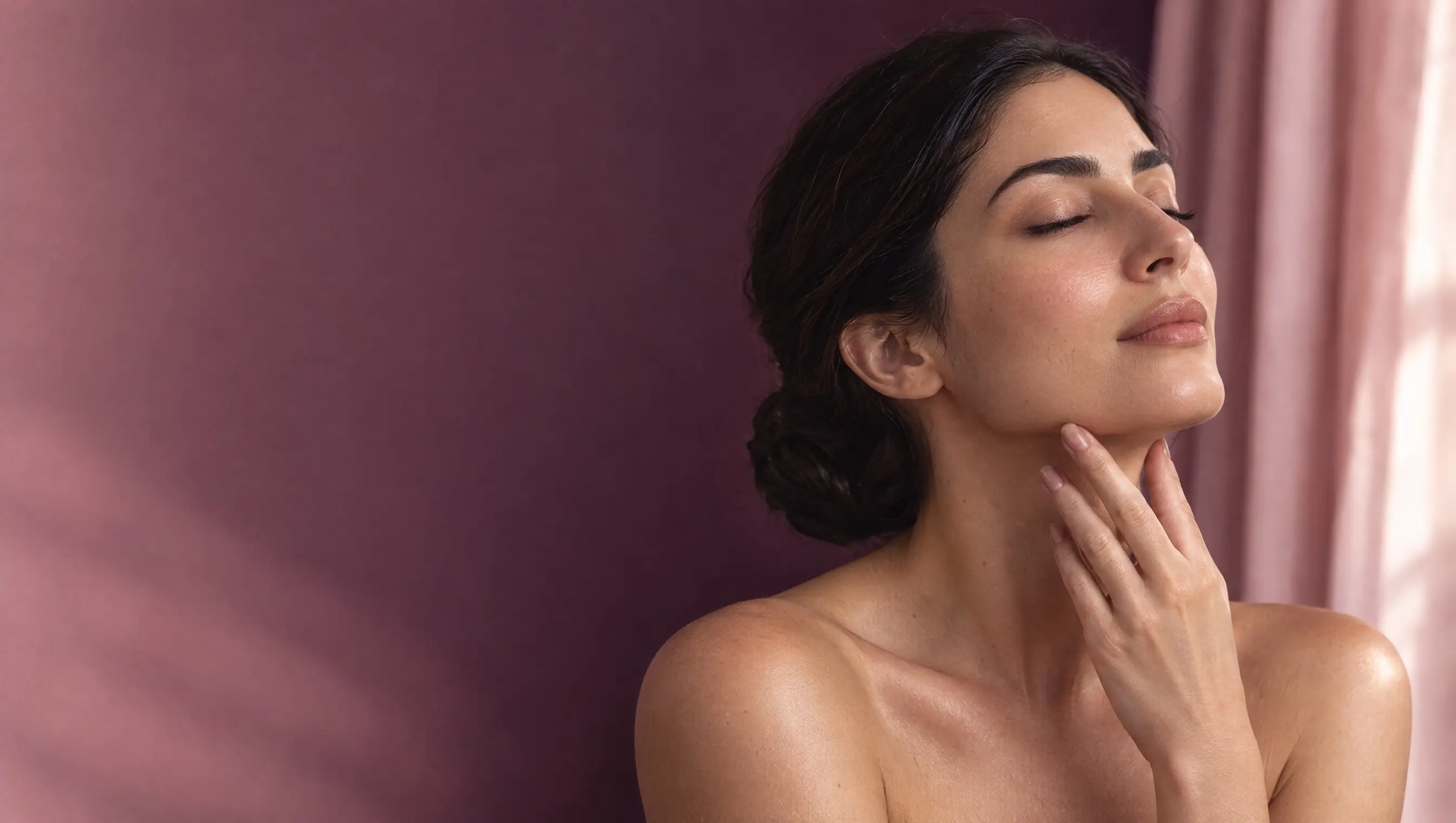 A woman with eyes closed and fingertips resting along her jaw, her skin glowing in warm light