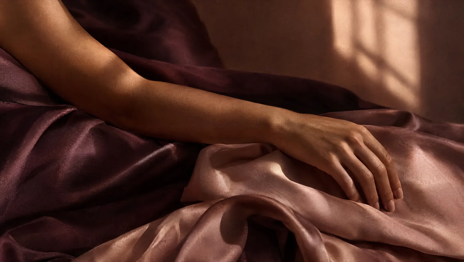 Warm olive skin on a forearm resting on folded plum silk in soft window light