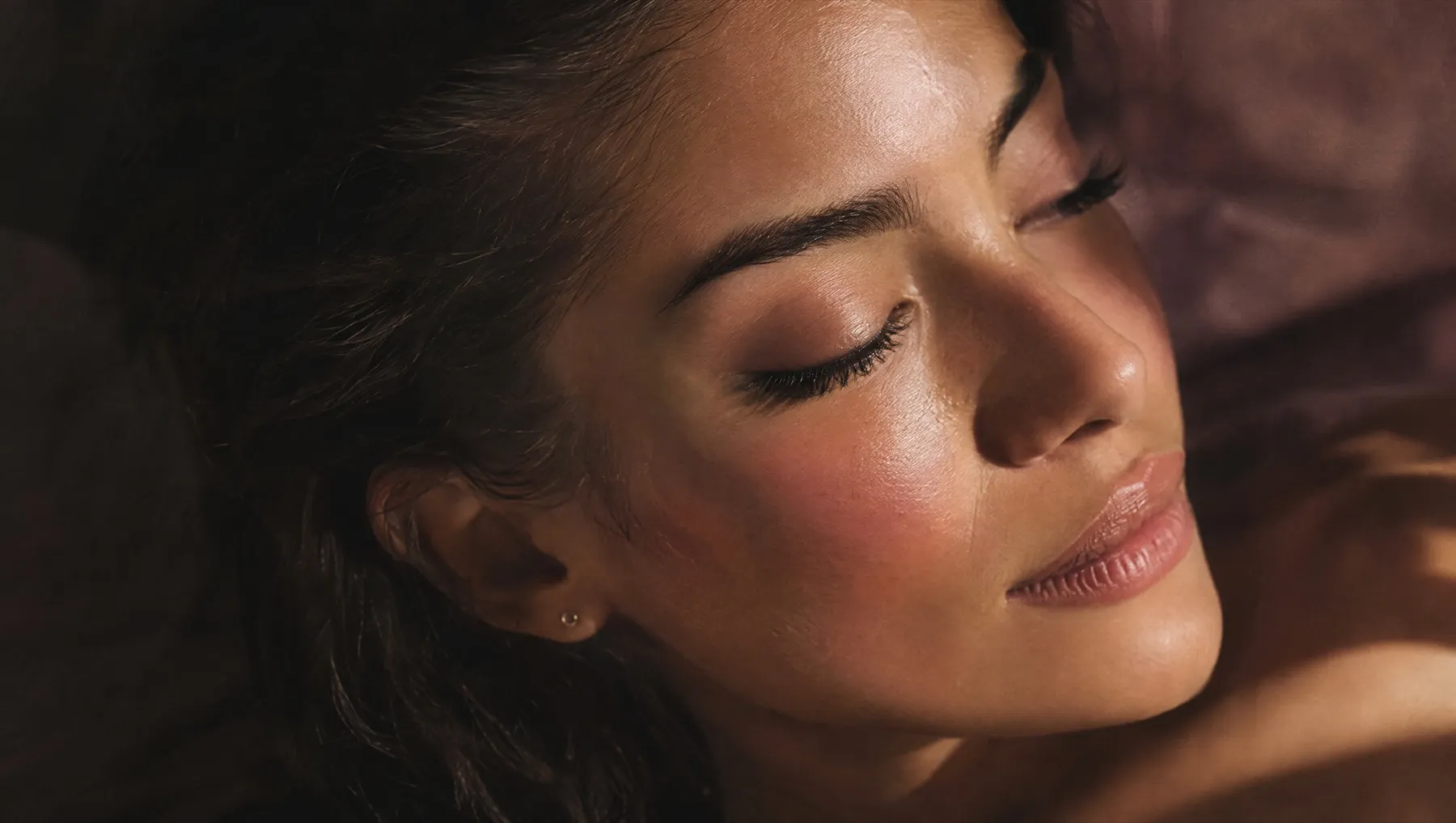 A woman with eyes closed and naturally curled dark lashes, in soft window light