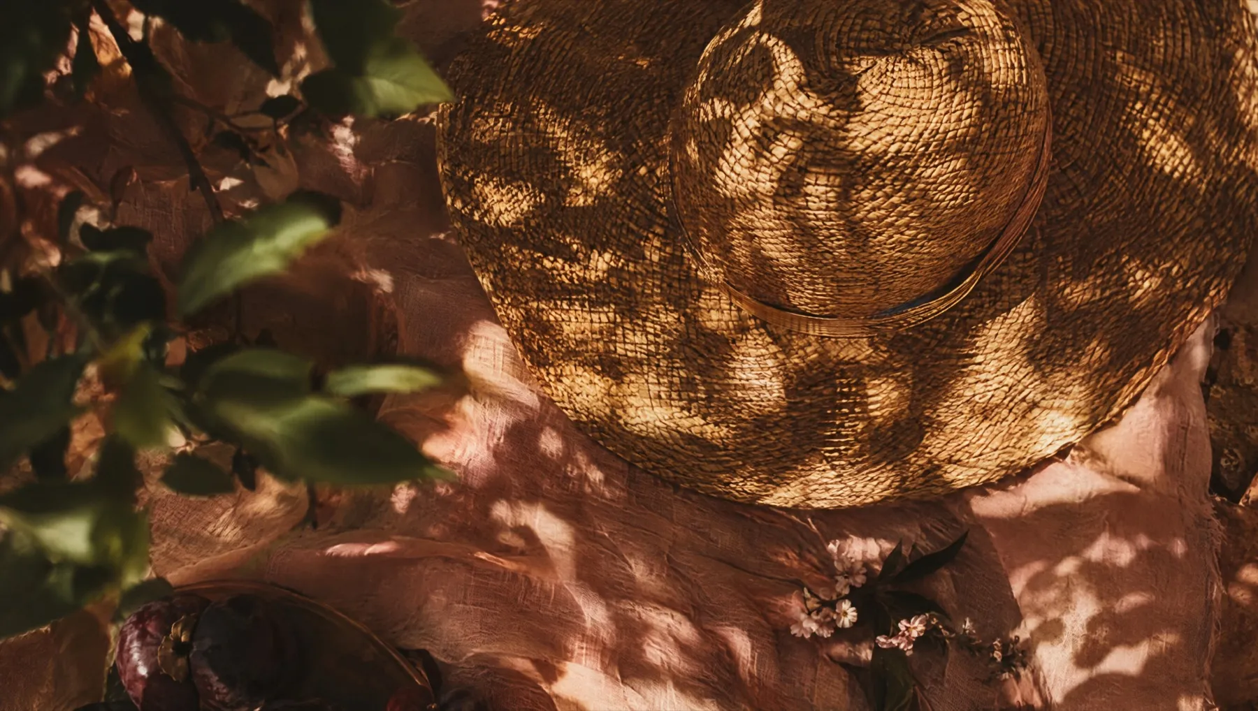 Dappled summer light falling across a blush linen sheet and a wide-brimmed straw hat
